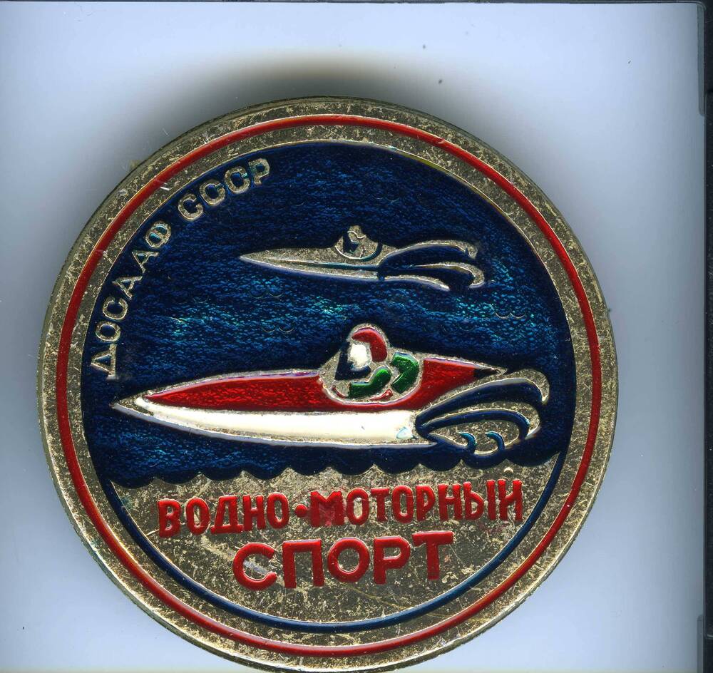 Значок Водно-моторный спорт - ДОСААФ СССР круглой формы, с изображением водной поверхности (синий цвет) и двух моторных лодок.