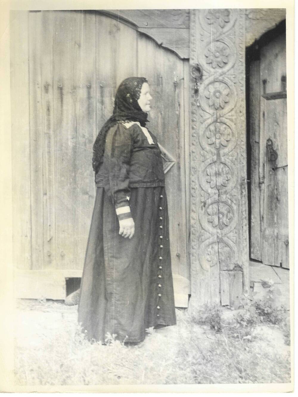 Фото портрет ростовой женщины в традиционном костюме около резной вереи дома.