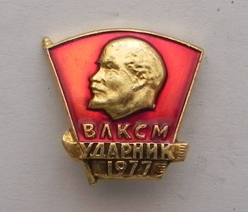 Значок ВЛКСМ Ударник 1977, четырёхугольной формы, зауженный к низу.