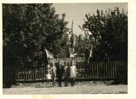 Фотопортрет групповой. Пять девочек стоят в ряд у забора на фоне памятника павшим в годы ВОВ