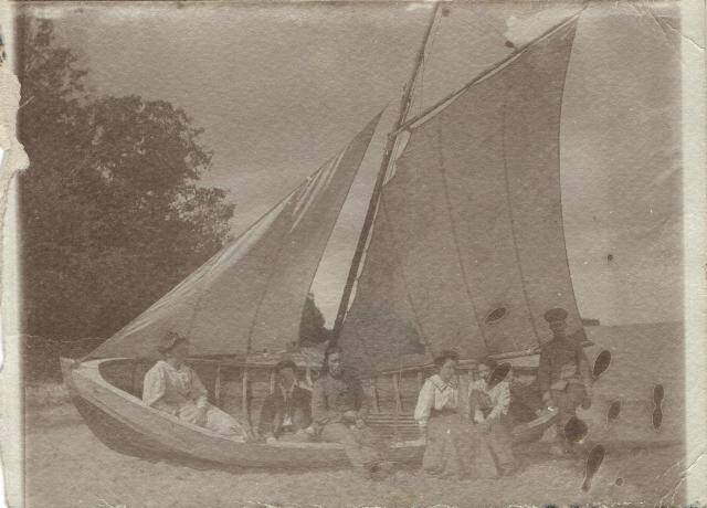 Фотография с изображением группы людей в парусной лодке на берегу.