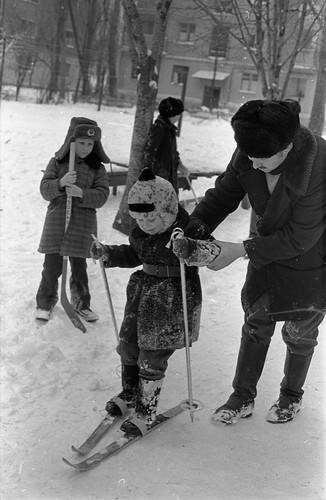 Негатив. В кадре мужчина учит ребенка кататься на лыжах.