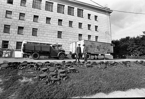 Негатив. В кадре двое мужчин в военной форме стоят на асфальтированной площадке возле трехэтажного здания.