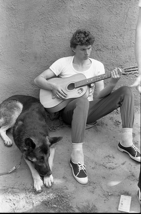 Негатив. В кадре юноша играет на гитаре, сидя на земле.