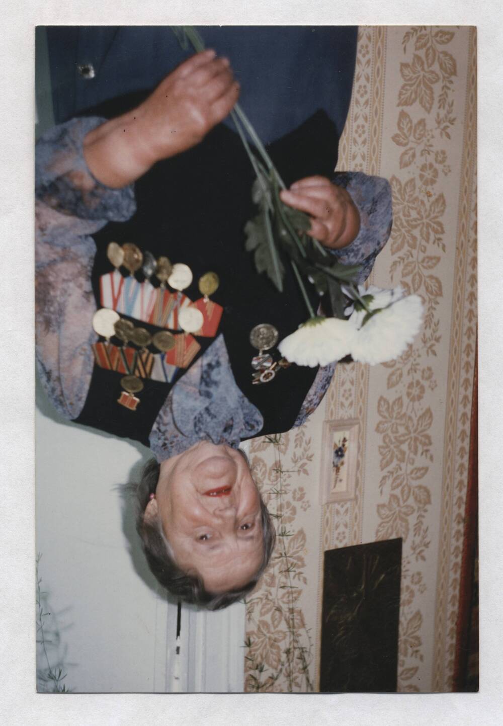 Фотография цветная. Изображена Степанцова М.А., стоящая в комнате с цветами в руках.