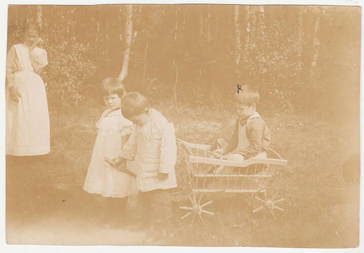 Фотография. Трое детей играют с тележкой на природе.