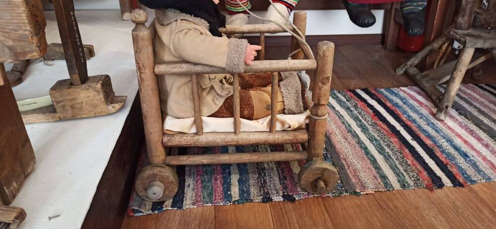 Коляска детская . Изготовлена из дерева, корпус имеет прямоугольную форму, стоит на четырех колёсах. Предназначена коляска  для передвижения маленьких детей . В переди прикреплена верёвка.