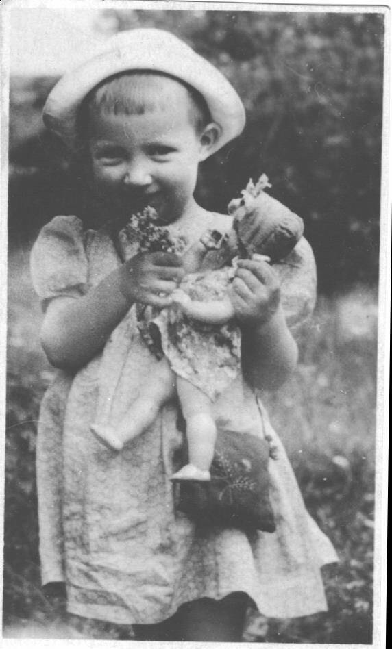 Малышка крепко держала кукол. Старое фото ребёнка на фоне кустов.