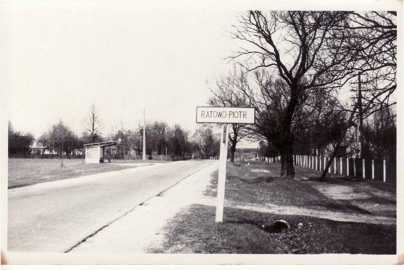 Фото ч/б. Улица в польской деревне с изображением указателя RATOWO-PIOTR (Ратов-Петрово) и остановки.