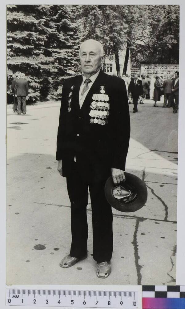 Фото в полный рост. Меренков Л.Л. в темном костюме, на пиджаке ордена и медали, в левой руке шляпа. 08.05.1989 г.
