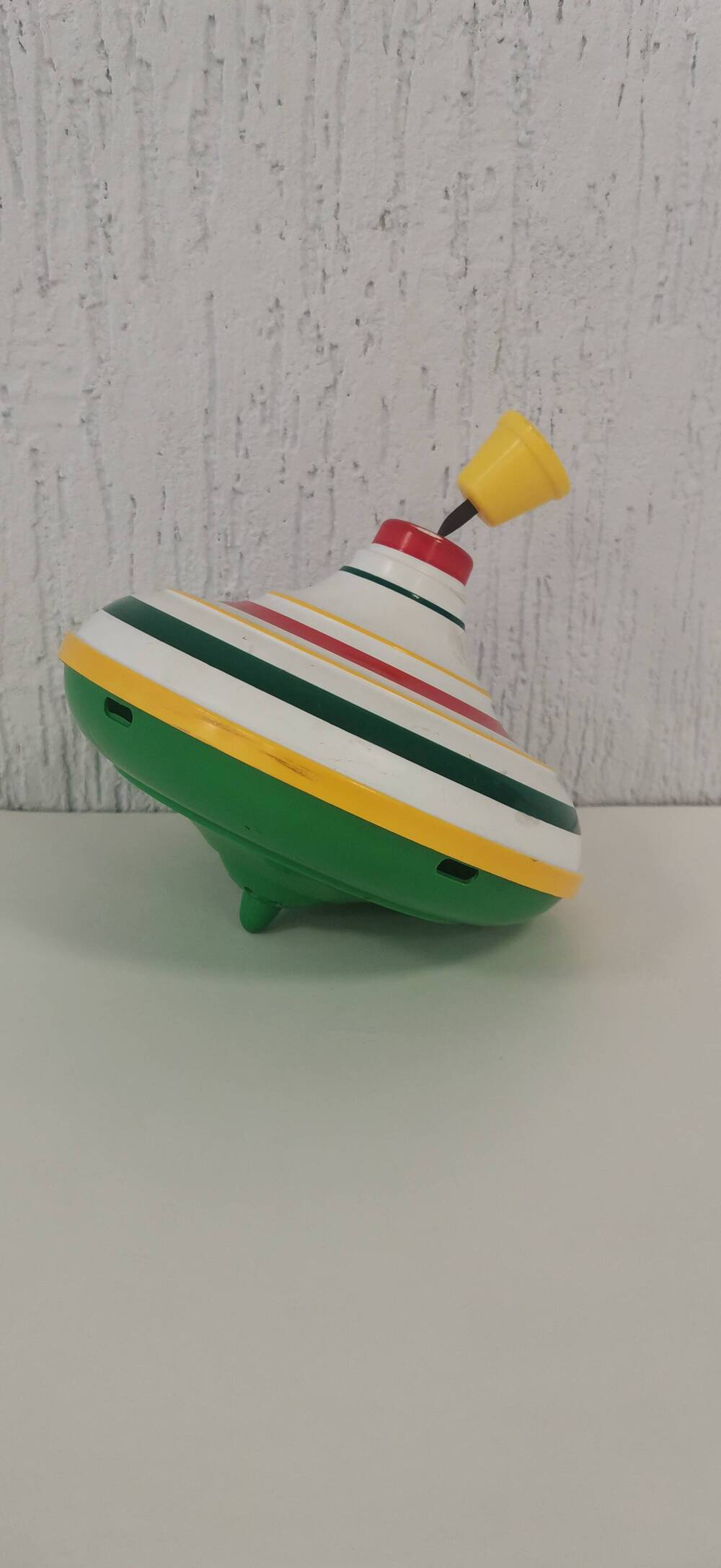 Игрушка Юла с запускателем. Материал пластмасса и металл. Цвет белый и зеленый с цветными полосами.