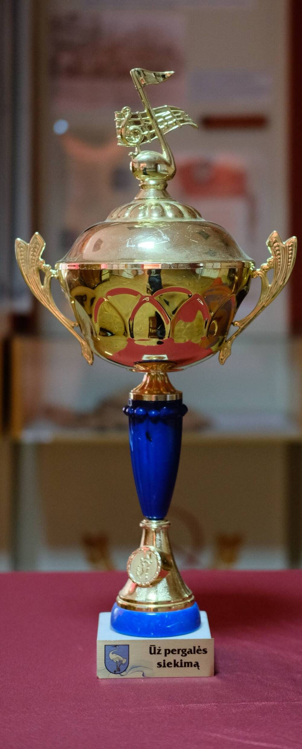 Кубок Uz pergales siekima Кубок в виде чаши золотистого цвета с орнаментами и фигурными ручками , на фигурной подставке