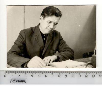 Фото сюжетное, по пояс. Ветеран Великой Отечественной войны Юсупов Н.Г.  сидит за столом и пишет ручкой.