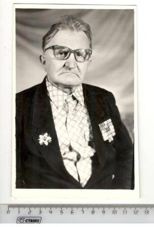 Фото участника войны Шакирова Ирека Ямалетдиновича. По пояс, в темном костюме, в клетчатой рубашке, на груди орденская планка, медаль, в очках.