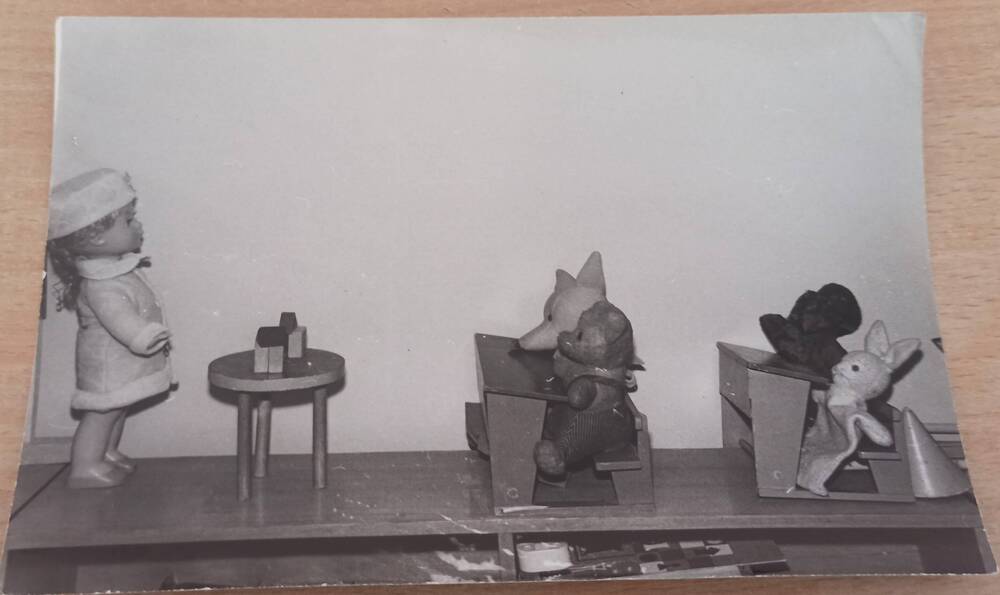 Фотография ч/б. Фрагмент стеллажа с игрушками сидящими за партами за партами г.Сковородино.