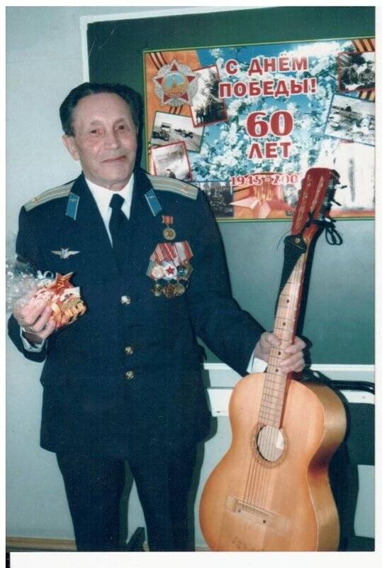 Фотография цветная. Борзов Владимир Ильич на фоне плаката «60 лет Победы».