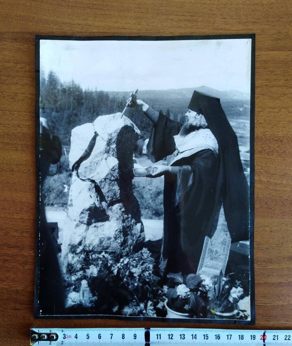 Фотография черно-белого цвета, глянцевая печать. Священнослужитель освещает памятник жертвам сталинских репрессий «Серпантинка»