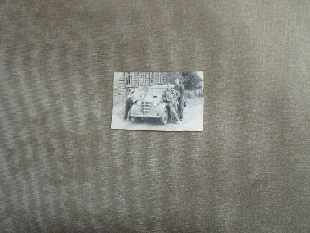 Фотография групповая: трое мужчин стоят, облокотившись на легковой автомобиль “Москвич”; сзади слева -деревянный дом (бревенчатый) с 4-мя окнами. Завод Красный пролетарий.  БАССР г. Стерлитамак. 1953 год.