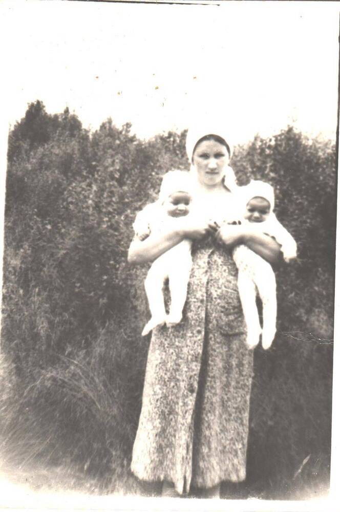 Молодая женщина держит в руках двух грудных малышей, в летнее время.