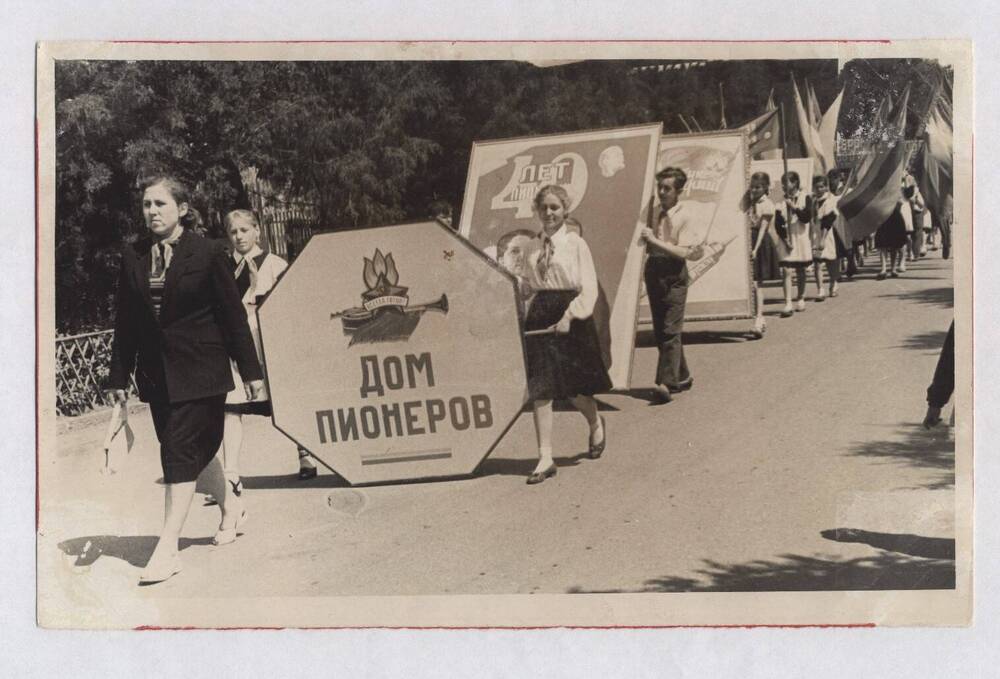Фотография черно-белая групповая. Изображена колонна пионеров, шагающая по дороге.