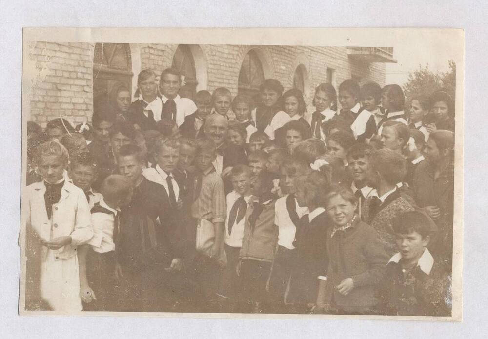 Фотография черно-белая групповая. Изображена группа пионеров, стоящих у здания с арочными окнами и балконом.