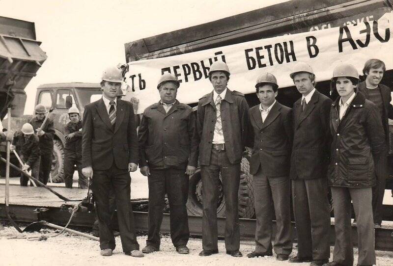 Фотография. Группа мужчин у плаката «Есть первый бетон в АЭС»