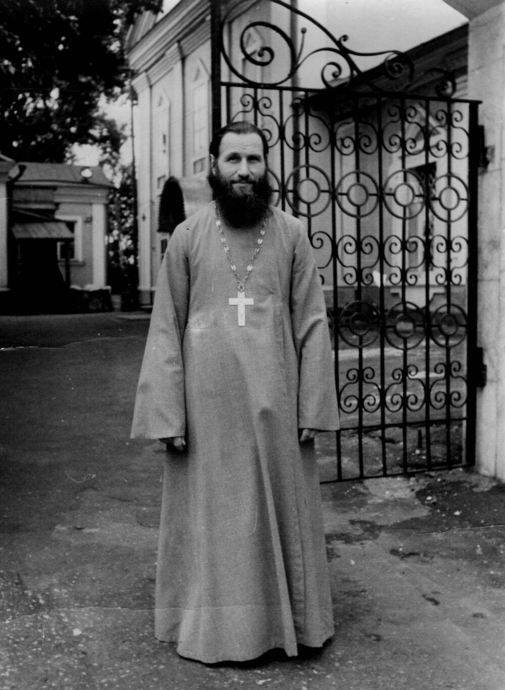 Фотография отца Геннадия в полный рост у ворот храма, в светлом облачении с наперсным крестом на груди, 1960-1970-е гг.