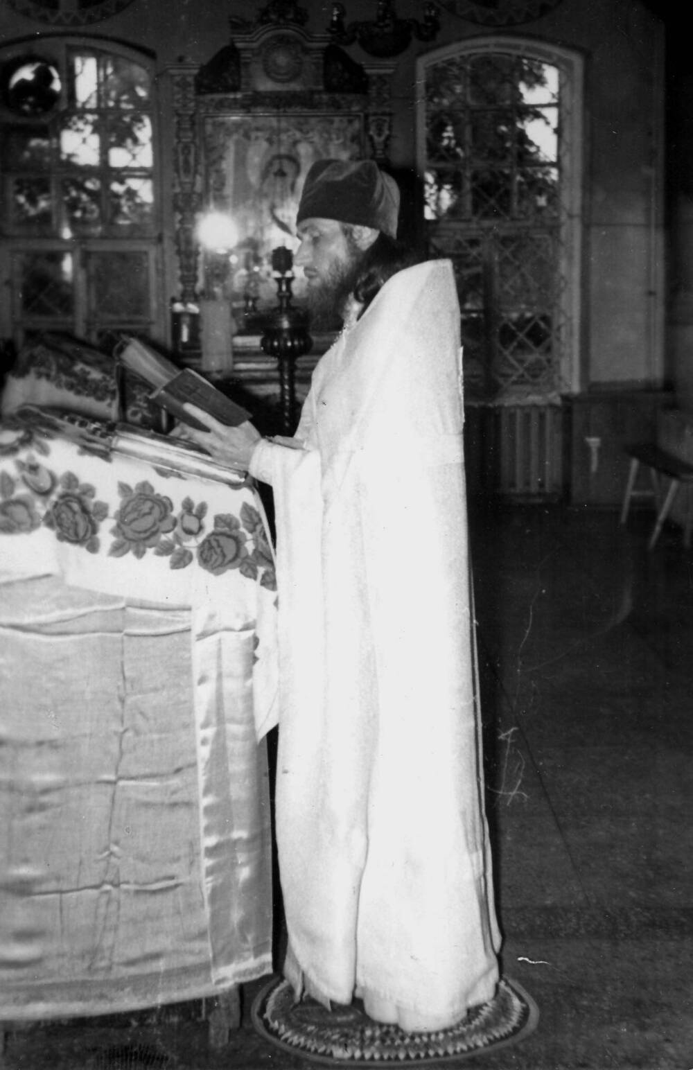 Фотография отца Геннадия у аналоя в полный рост в светлом облачении, с открытой книгой в руках, в храме Сретение Господня, 
1990-е гг.