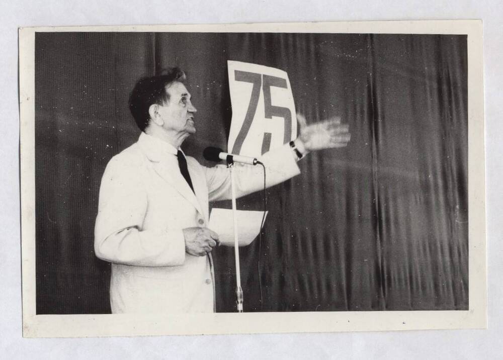 Фотография черно-белая. Изображен В.А. Нашивочников, стоящий на сцене у микрофона.