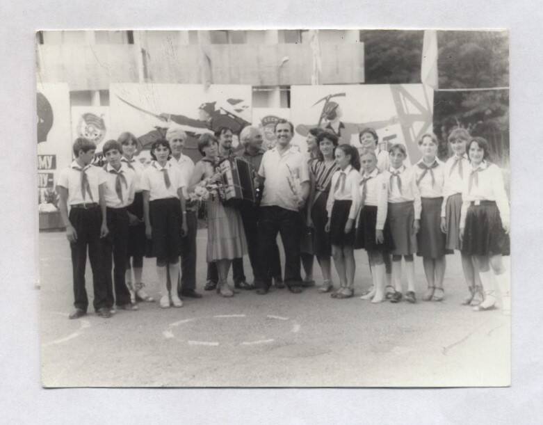 Фотография черно-белая, групповая. Изображен В.А. Нашивочников с букетом гладиолусов в руках среди пионеров.