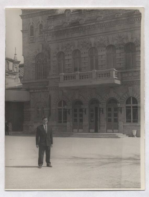 Фотография черно-белая. Изображен  В.А. Нашивочников, стоящий у старинного многоэтажного здания.