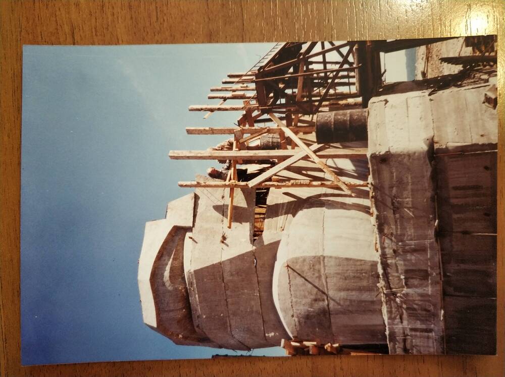 Фотография цветная, глянцевая печать. Строительство монумента «Маска Скорби». Нижняя лицевая часть монумента, окруженная строительными лесами и архитектор Камиль Козаев, г. Магадан, 1990-е гг.