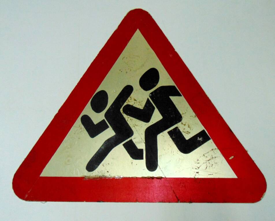 Дорожный знак в виде белого треугольника с красной каймой и изображением бегущих детей - предупреждающий знак Дети, устанавливается на участке дороги вблизи детского учреждения. 1996 г.