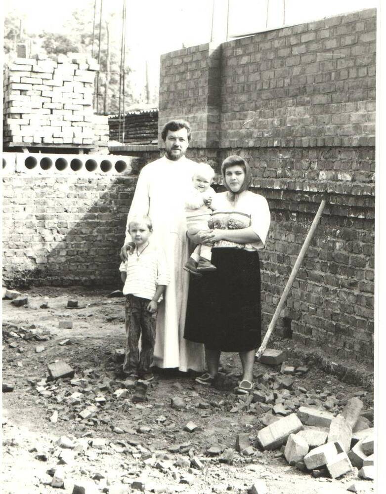 Фотография черно-белая. Г.М. Самойленко с семьей на строительстве нового храма.  На заднем плане стена с бетонным перекрытием и сложенным кирпичом.