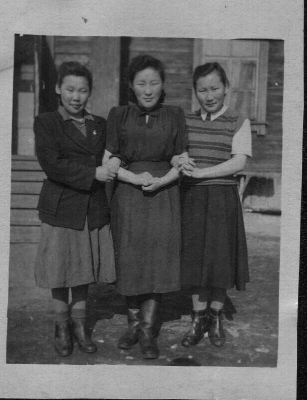 Фотография черно-белая групповая. На фоне деревянного здания 3 неизвестные девушки.