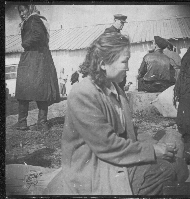 Фотография черно-белая групповая. Неизвестная девушка в профиль на бревне, на заднем женщина-якутка, мужчина русский в фуражке. Двое мужчин сидят спиной.