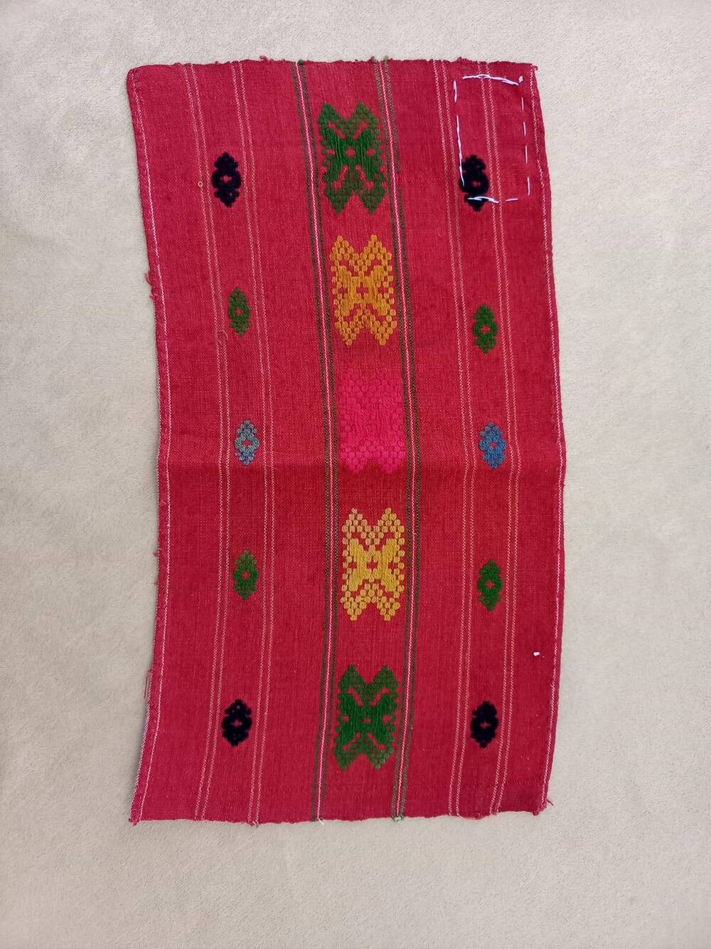 Национальная вышивка на куске красного домотканного холста . Вышивка разноцветная.