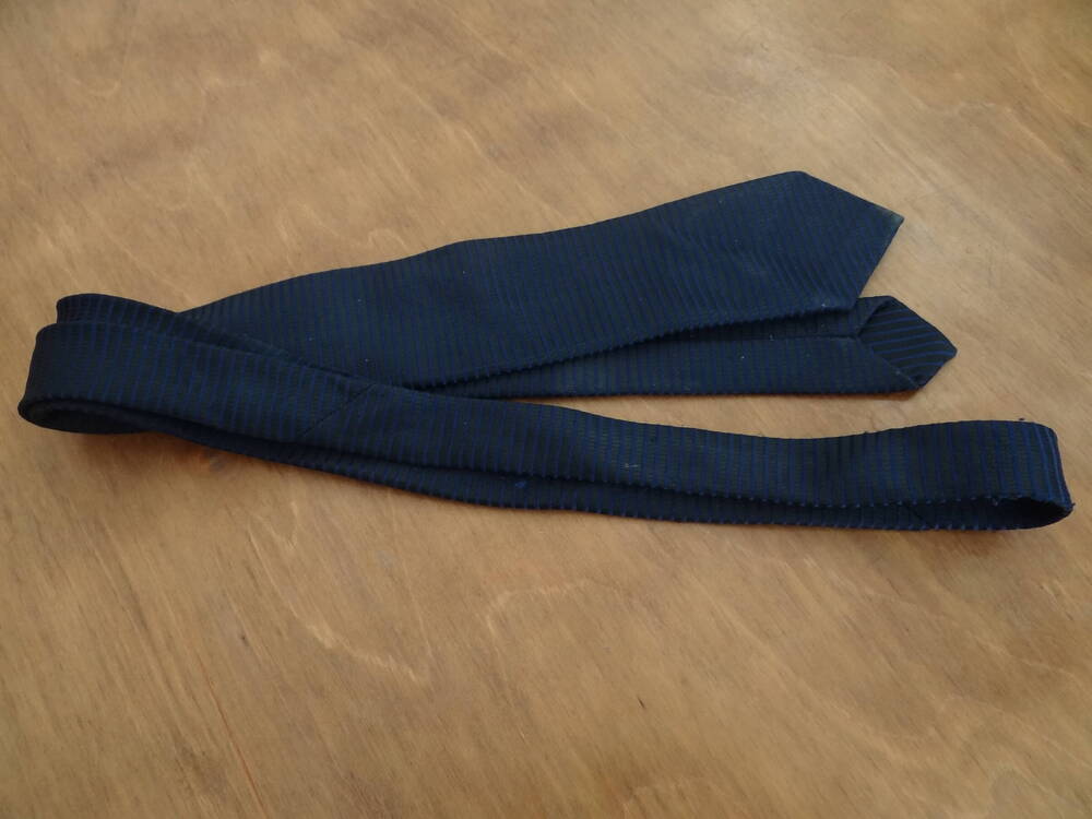 Галстук мужской синего цвета с черными полосками. Галстук имеет вытянутую форму. На задней стороне находится логотип с тремя буквами: ЩТФ