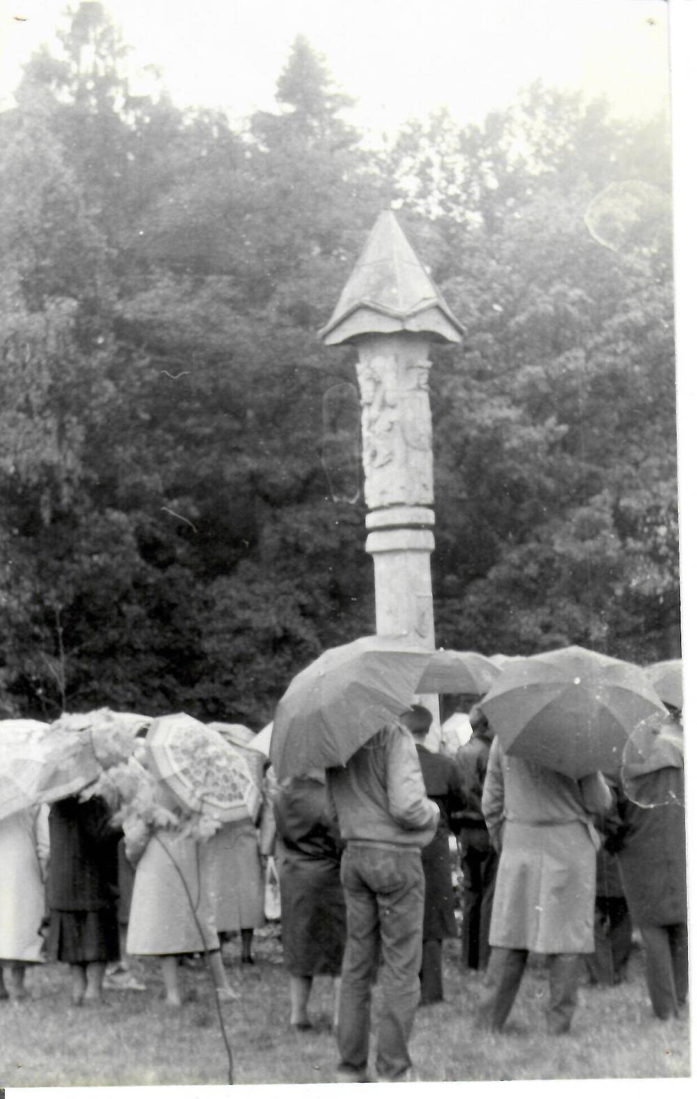 Фотография, черно-белая, глянцевая печать. Группа людей с зонтами стоит перед столпом (традиционный деревянный алтарь Литвы).