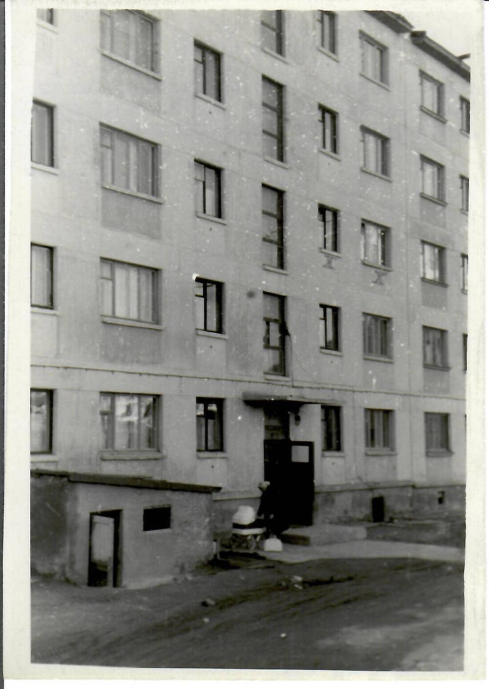 Фотография черно-белая, глянцевая печать. На фото: вид на пятиэтажный дом. У подъезда женщина с коляской, г. Магадан, 1966 г.
