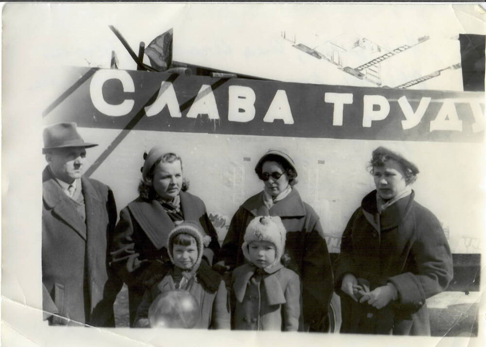 Фотография черно-белая, полуматовая печать. На фото: группа людей на первомайской демонстрации на фоне надписи «Слава труду», из них: один мужчина, три женщины и два ребенка. г. Магадан, 1960 г.