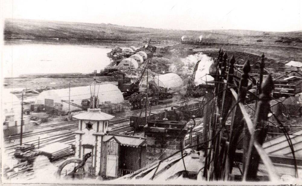 Фото ч/б документальное. Фото сделано с крыши здания морского вокзала в 1951 года. На снимке вид порта Ванино, видны склады размещенные по береговой части бухты. 