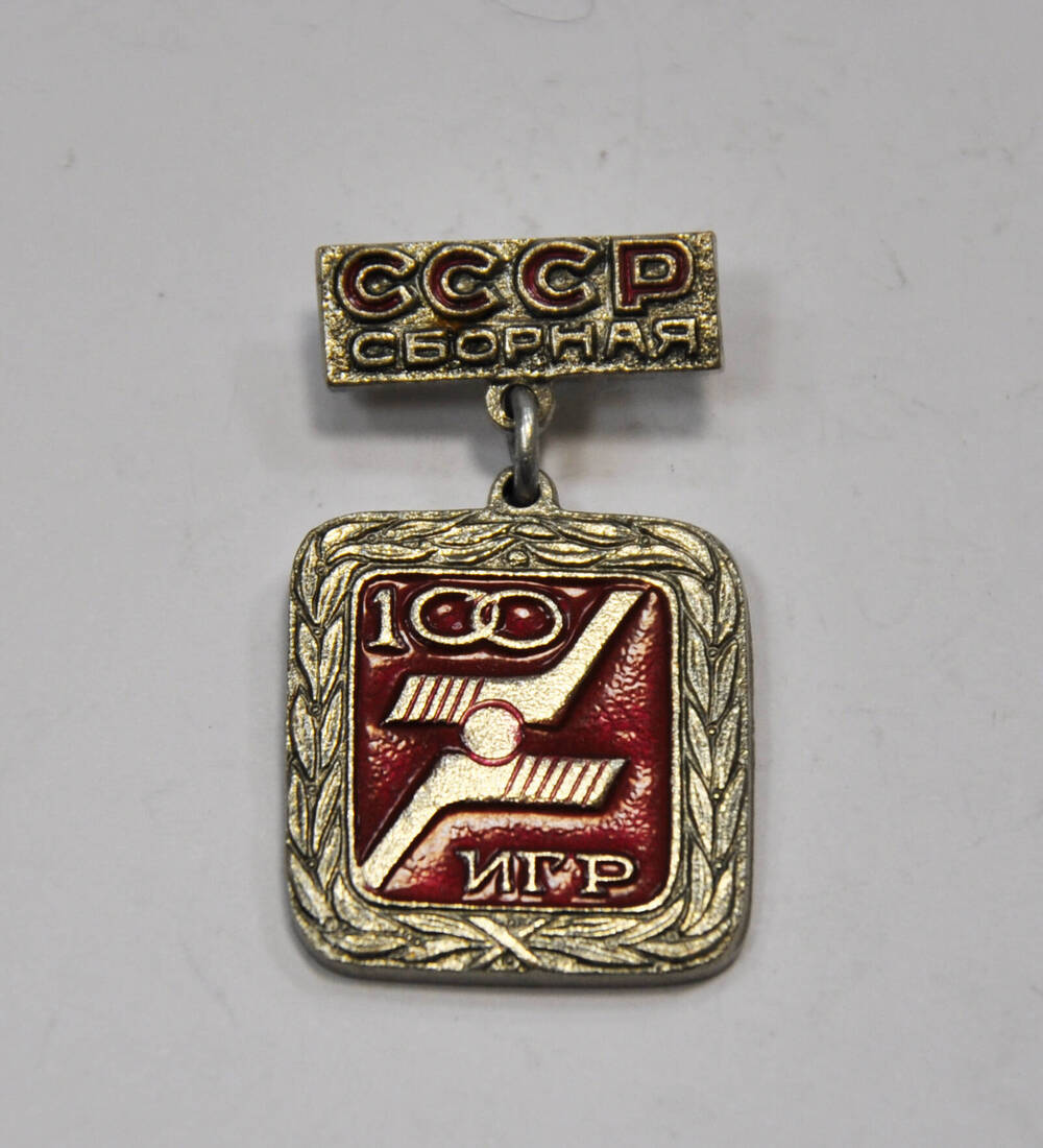 Знак 100 игр за сборную СССР по хоккею. Знак квадратной формы с  закругленными углами, из металла белого цвета. Знак кольцом крепится к  прямоугольной п 21 век