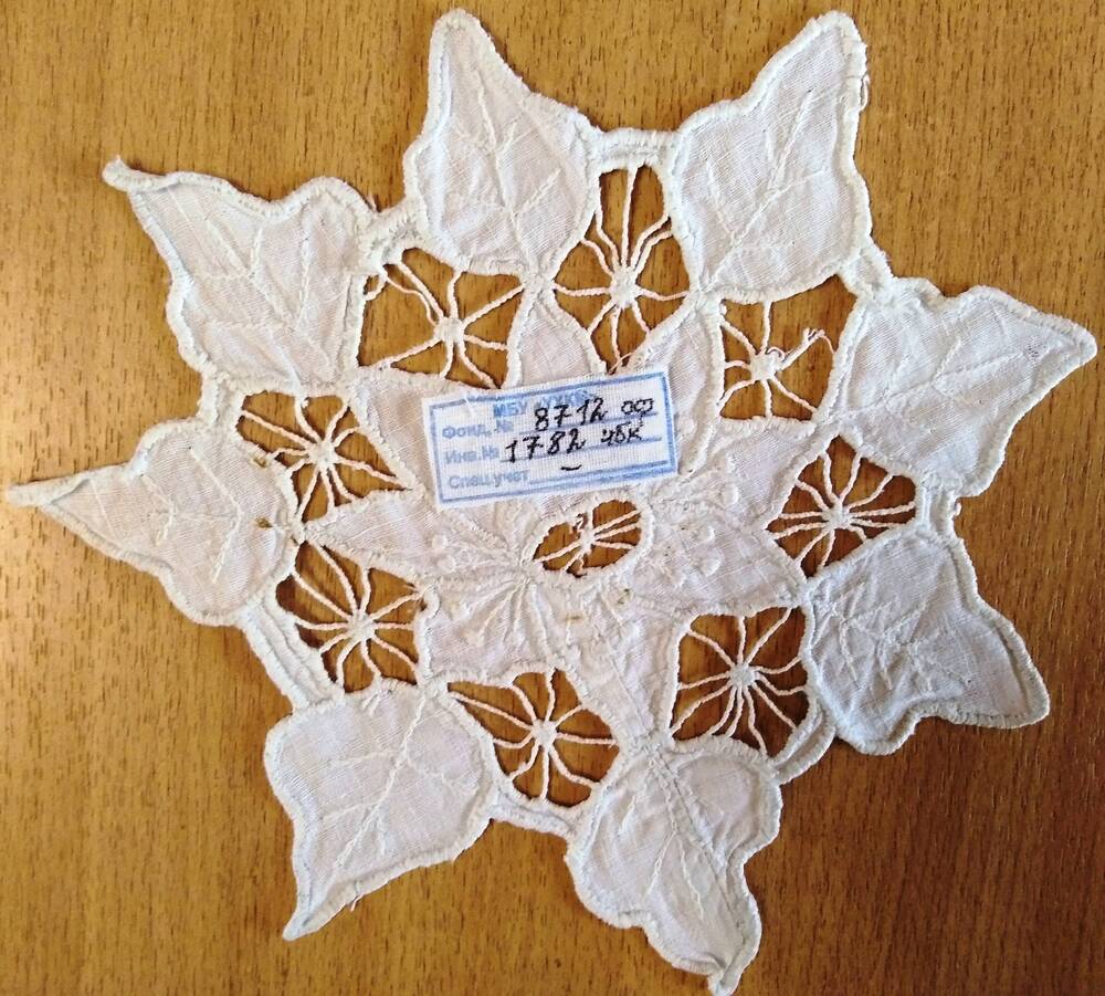Салфетка из х/б ткани ажурная, белого цвета округлой формы, выполнена в технике «ришелье» (орнамент цветочно-растительный). Края резные, игольчатые. Элементы внутри салфетки соединены между собой сетчатым орнаментом из нитей.