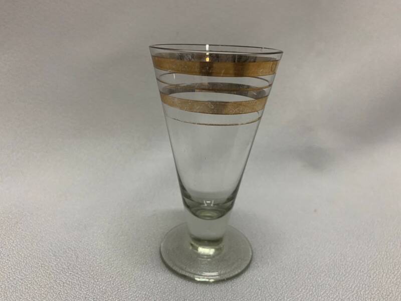 Рюмка  для спиртных напитков, стеклянная, прозрачная, декорирована двумя горизонтальными чередующимися широкими и тонкими золотистыми полосами.