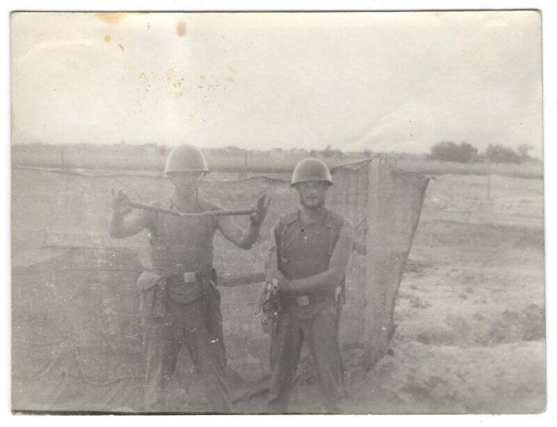 Фотография: Два военнослужащих Советской Армии в касках и бронежилетах на фоне газопровода. Афганистан