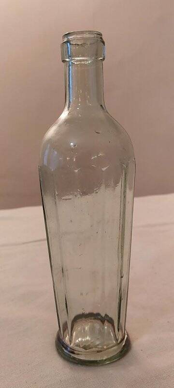Бутылка прозрачного сероватого стекла с 12 гранями. Тулово сужается к низу, дно плоское, горло короткое.