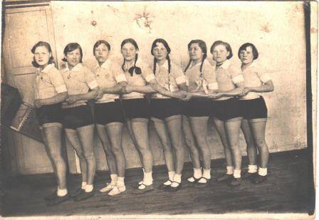 Фотография черно-белая. Шильникова А. в спортивной форме с группой девочек стоит  у стены