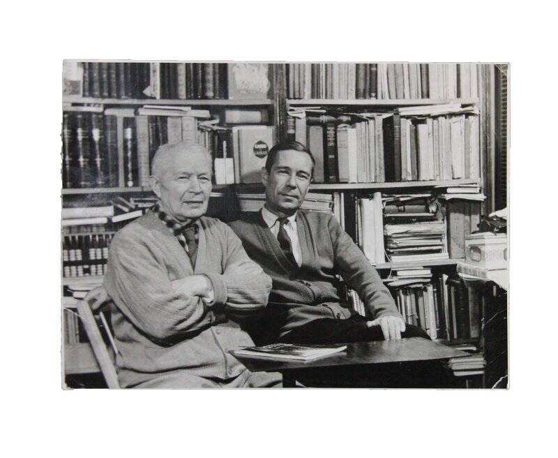 Фотография ч/б. Тюрин А.В. сидит рядом с мужчиной на фоне библиотеки