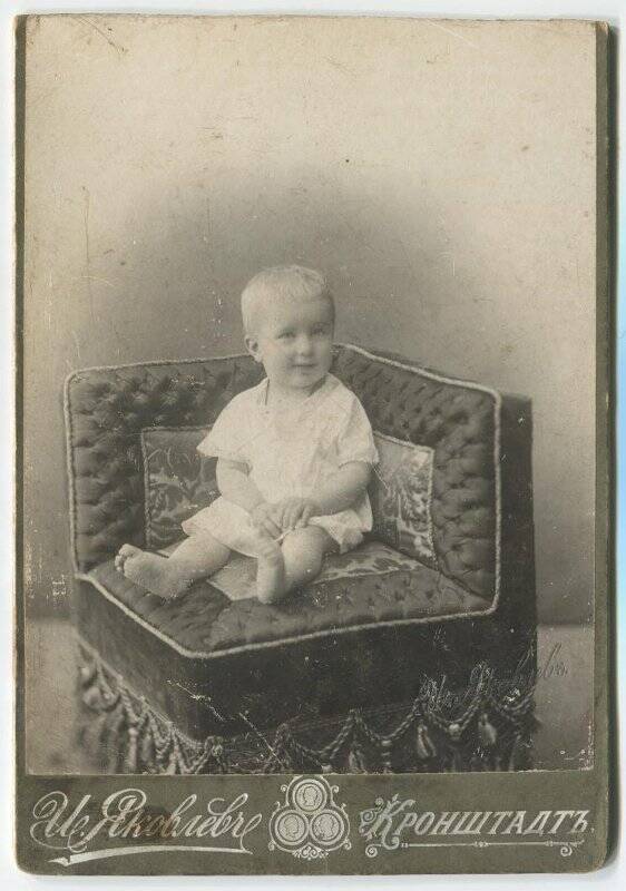 Фотография черно-белая с изображением ребенка, сидящего на угловом кресле-диване.